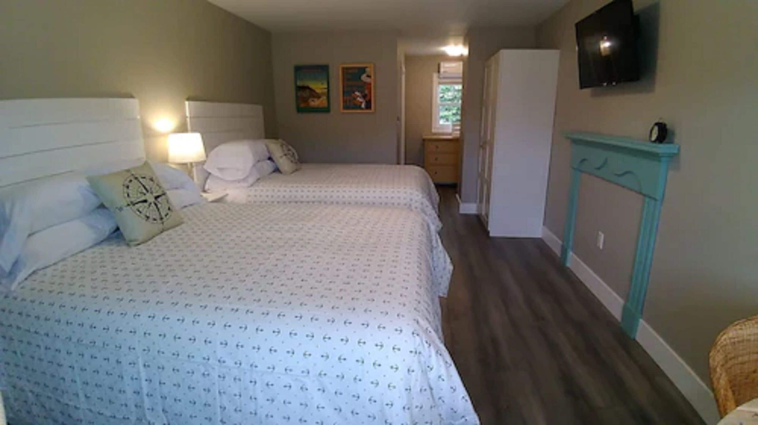 Een slaapkamer met twee bedden, een aan de muur bevestigde televisie en een klein kastje.