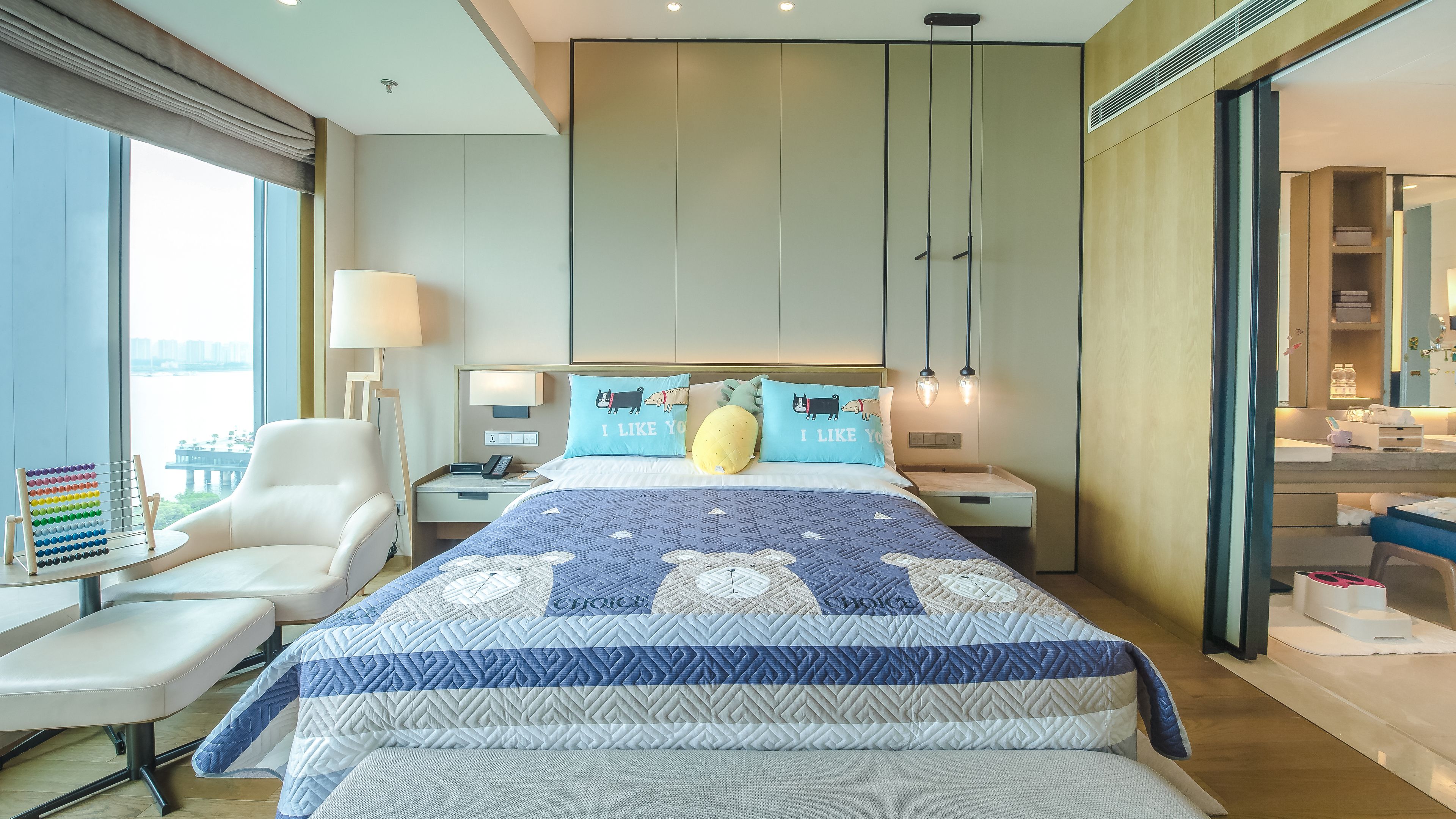 Habitación de hotel moderna con una cama grande, un escritorio con lámpara y vistas a una masa de agua.