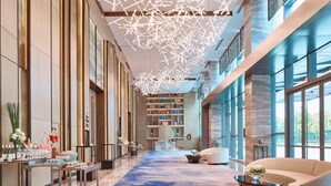 Un amplio vestíbulo de hotel con alfombra azul, una recepción, un sofá y una mesita de centro.