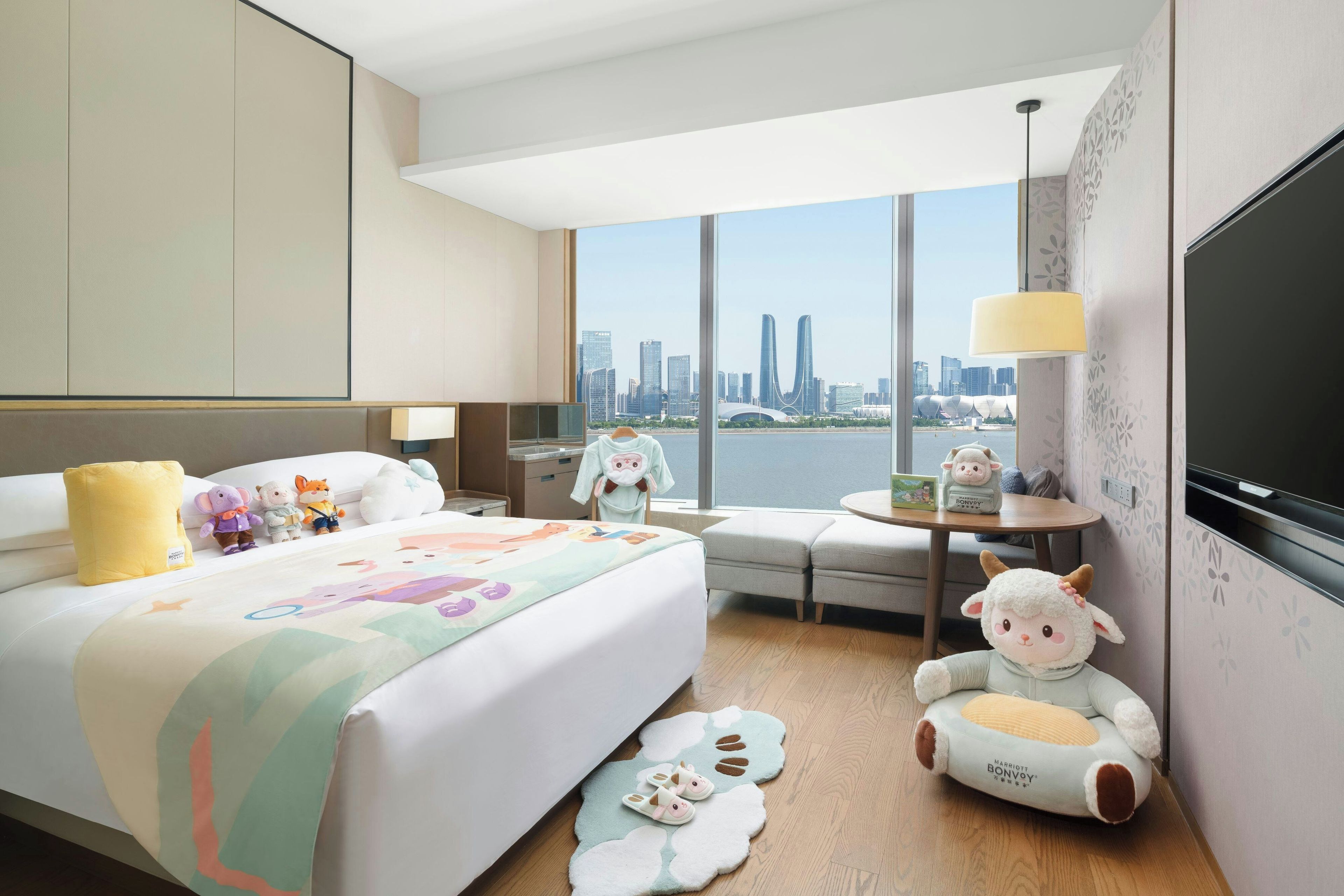 A hotel room with a large bed, a desk, a chair, a TV, and a view of a city skyline.