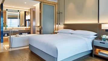 Une chambre d’hôtel moderne dotée d’un grand lit, d’une salle de bain séparée, d’une coiffeuse avec un miroir et d’une table de chevet avec une lampe.