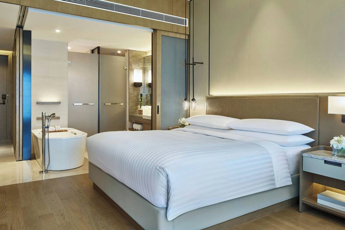 Una habitación de hotel moderna con una cama grande, baño independiente y una mesita de noche pequeña.