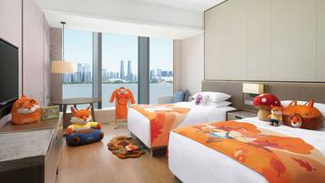 A hotel room with two beds, a desk with a television, and a view of a city skyline.