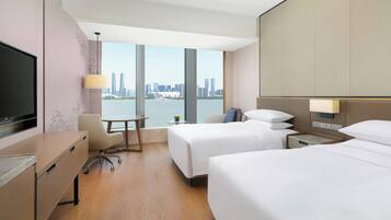 Una habitación de hotel con escritorio, dos camas, televisor y vista a la ciudad.