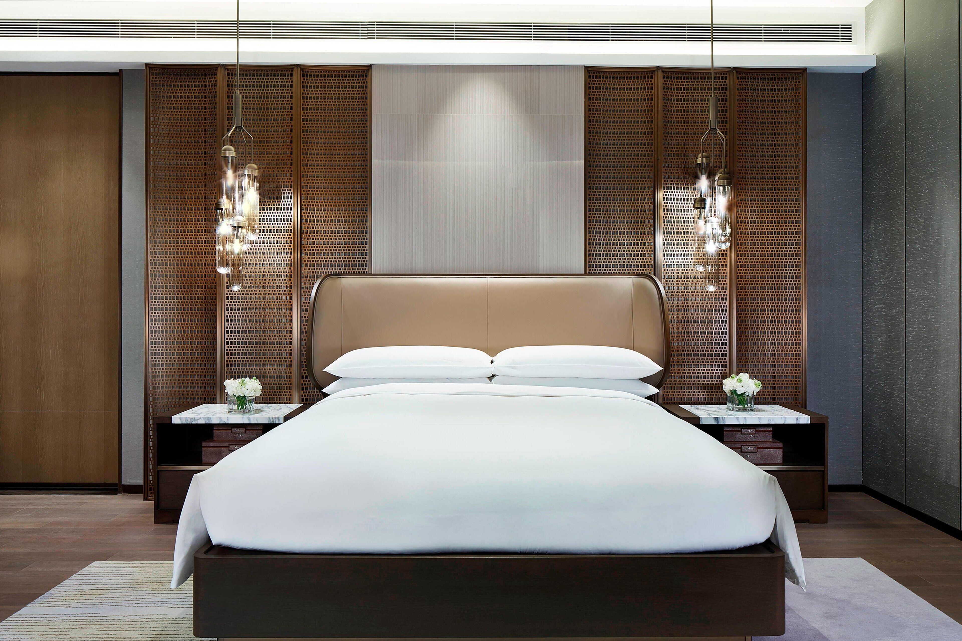 Une chambre moderne avec un grand lit, une tête de lit en bois et deux tables de chevet ornées de lampes décoratives.