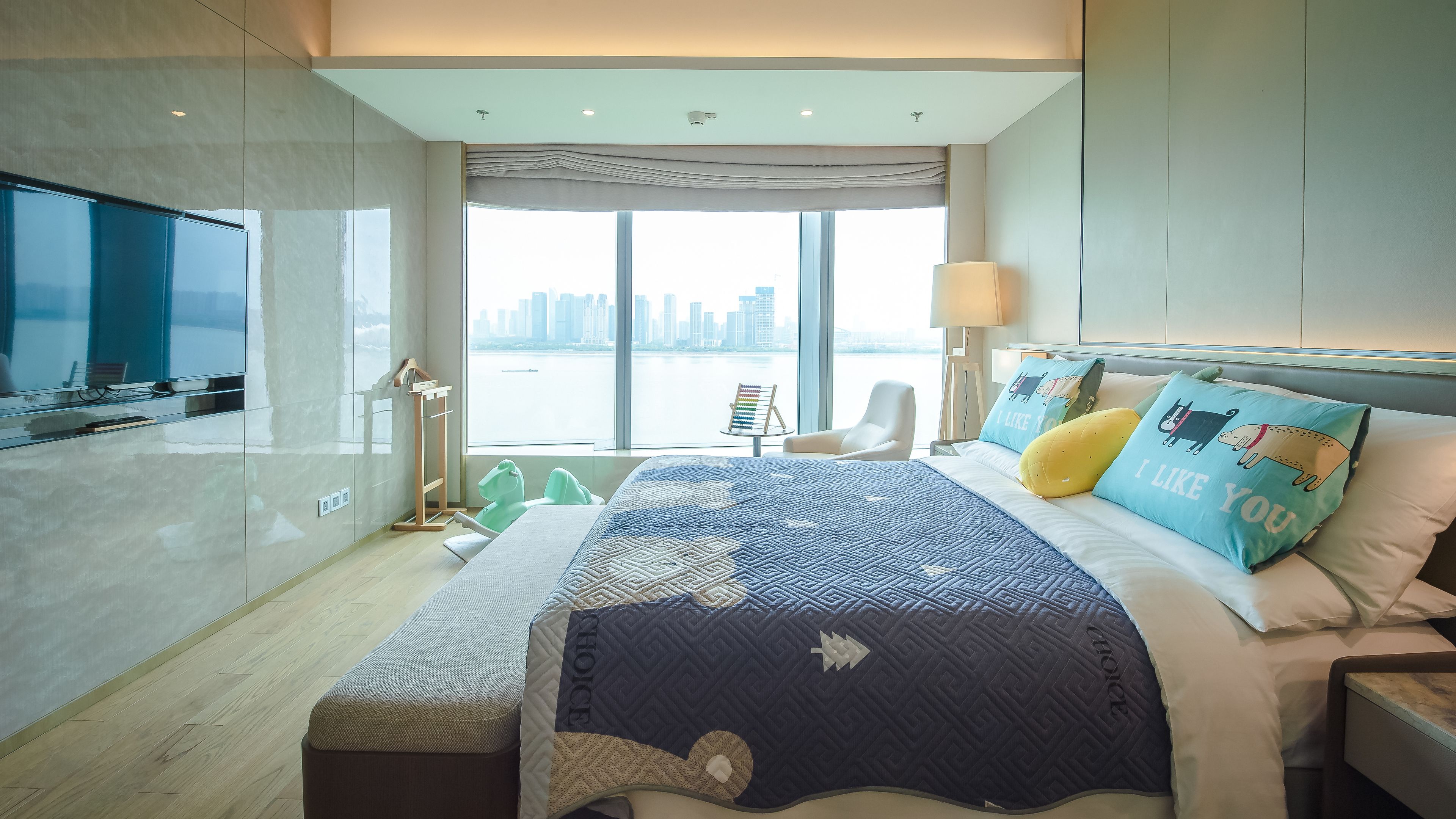 A modern hotel room with a large bed, a TV, a view of the city, and a balcony.