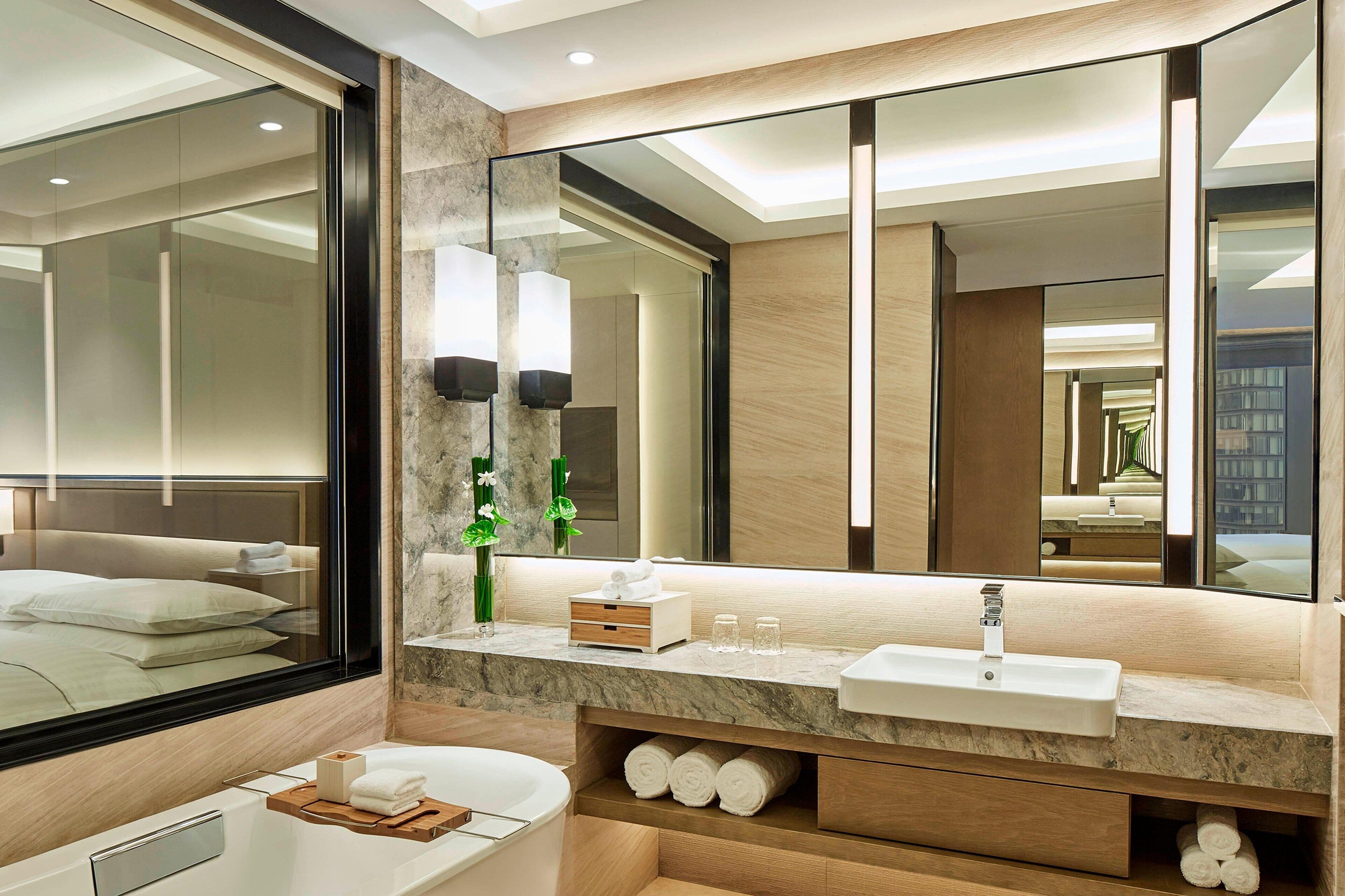 A modern bathroom with a large mirror, a bathtub, and a vanity with a sink.