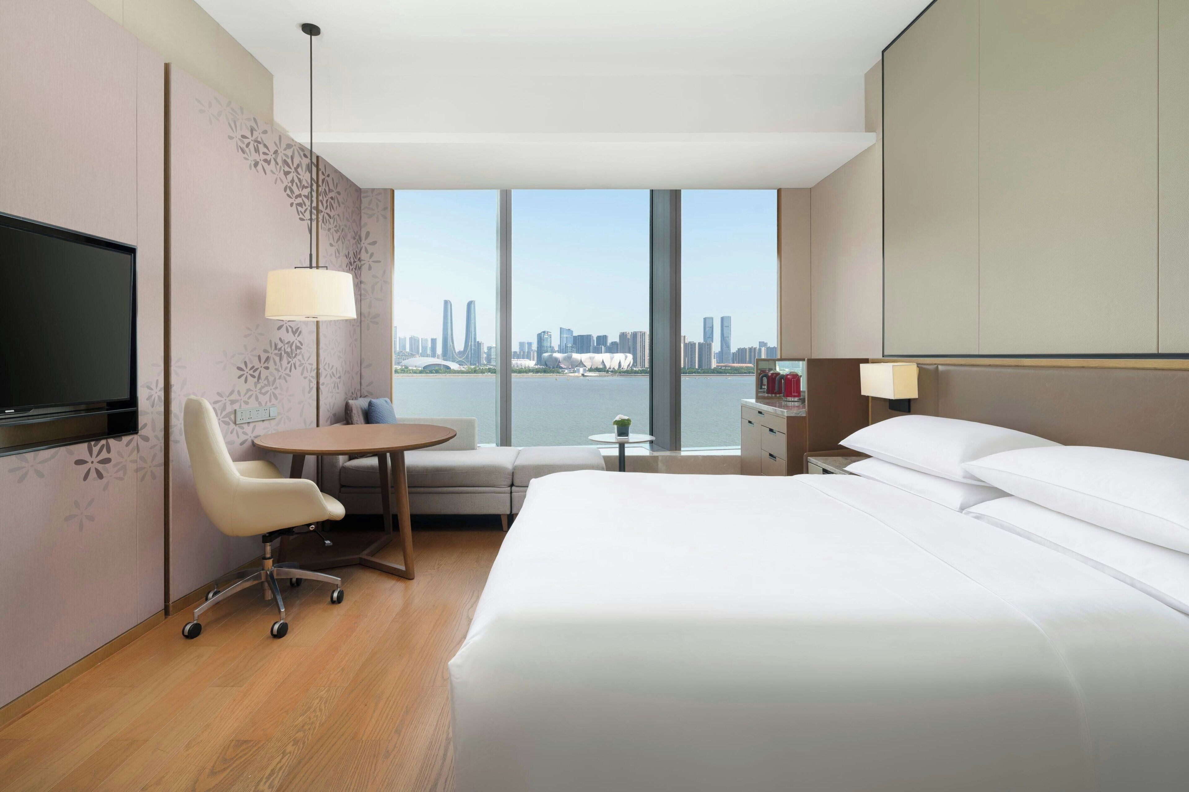 Una camera d'albergo con un letto, una scrivania, una sedia, una televisione, una lampada e vista sullo skyline cittadino.