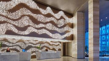 Un moderno vestíbulo de hotel con un gran diseño mural iluminado, una recepción y vistas de la ciudad a través de amplias ventanas.