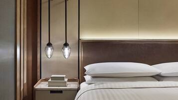 A neatly made bed with white linens and a headboard, a bedside table with books, and a hanging light fixture.