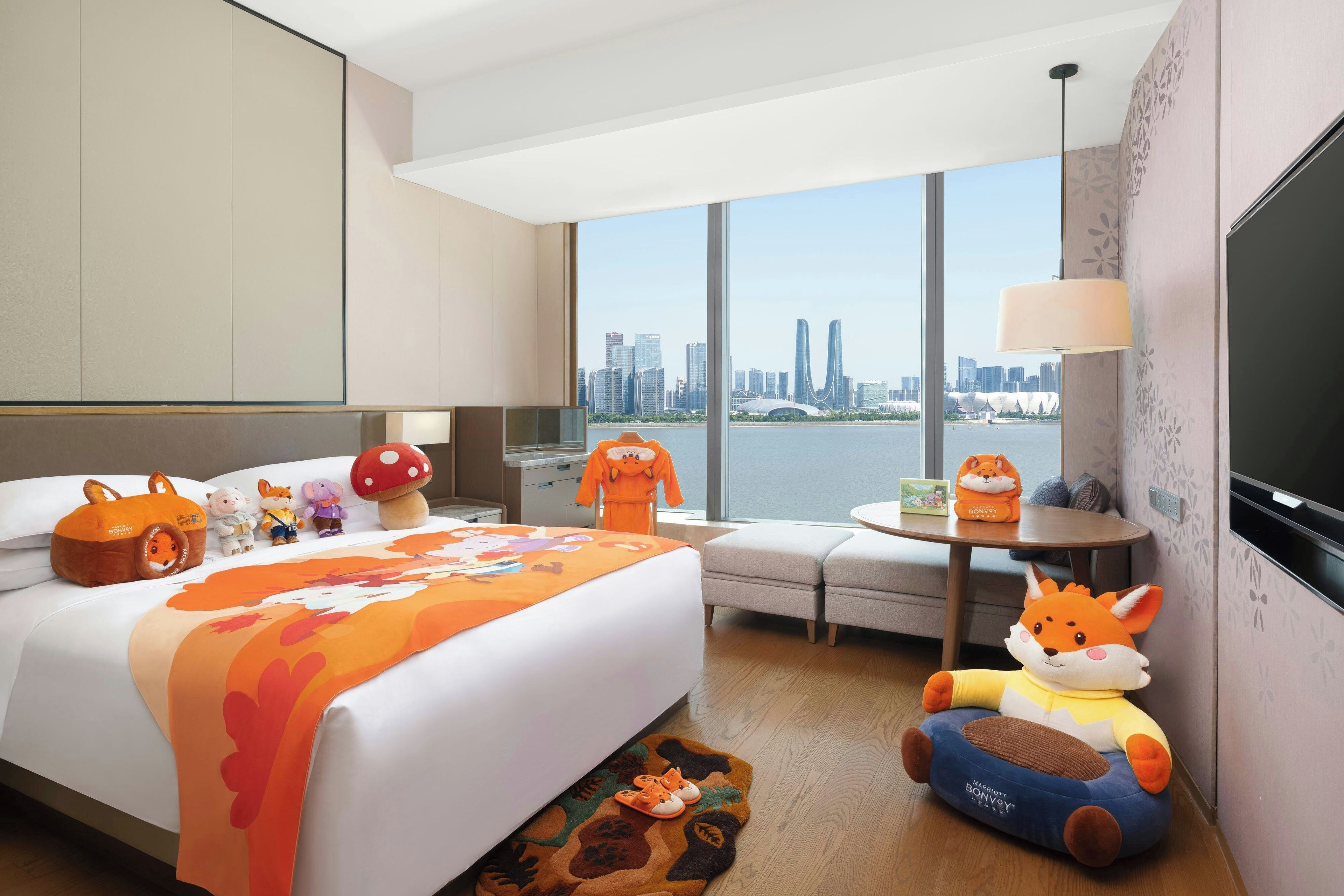 A hotel room with a large bed, a sofa, a table with a lamp, and a view of a city skyline.