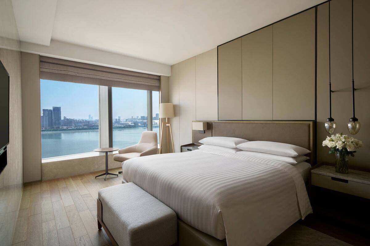 Una habitación de hotel moderna con una cama grande, una zona de estar, una mesita de noche y vistas a la ciudad.