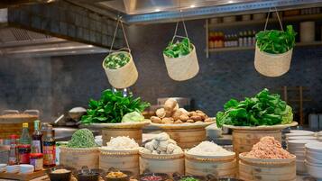 A variety of Asian noodle dishes displayed in wooden baskets, with hanging baskets of fresh greens and condiments on the side.