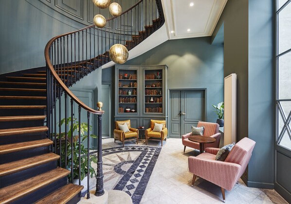 Un magnifique escalier en bois, agrémenté de rampes noires, mène à une bibliothèque dotée d’étagères et de deux fauteuils.
