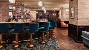 A bar area with multiple stools, a bookshelf, and a counter. - The Hoxton, Paris (Paris)