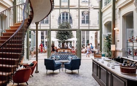 A spacious indoor area with a curved staircase, a seating area with blue sofas, and a bar with bottles.