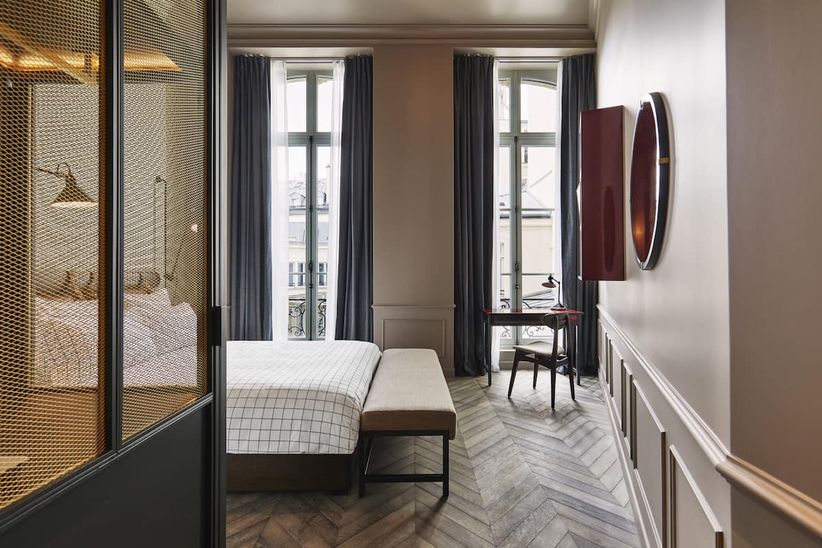 Een hotelkamer met een bed, een bankje, een bureau en grote ramen.