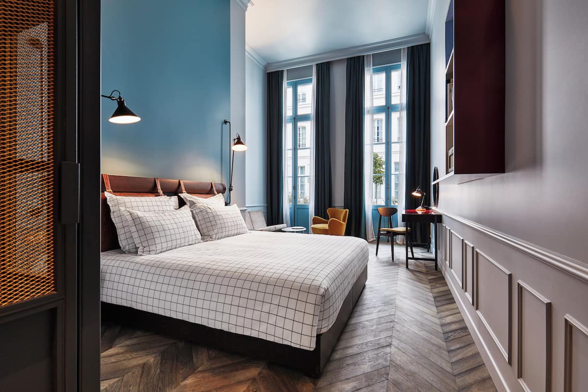 Een slaapkamer met een bed, een stoel, een bureau en een raam met gordijnen.