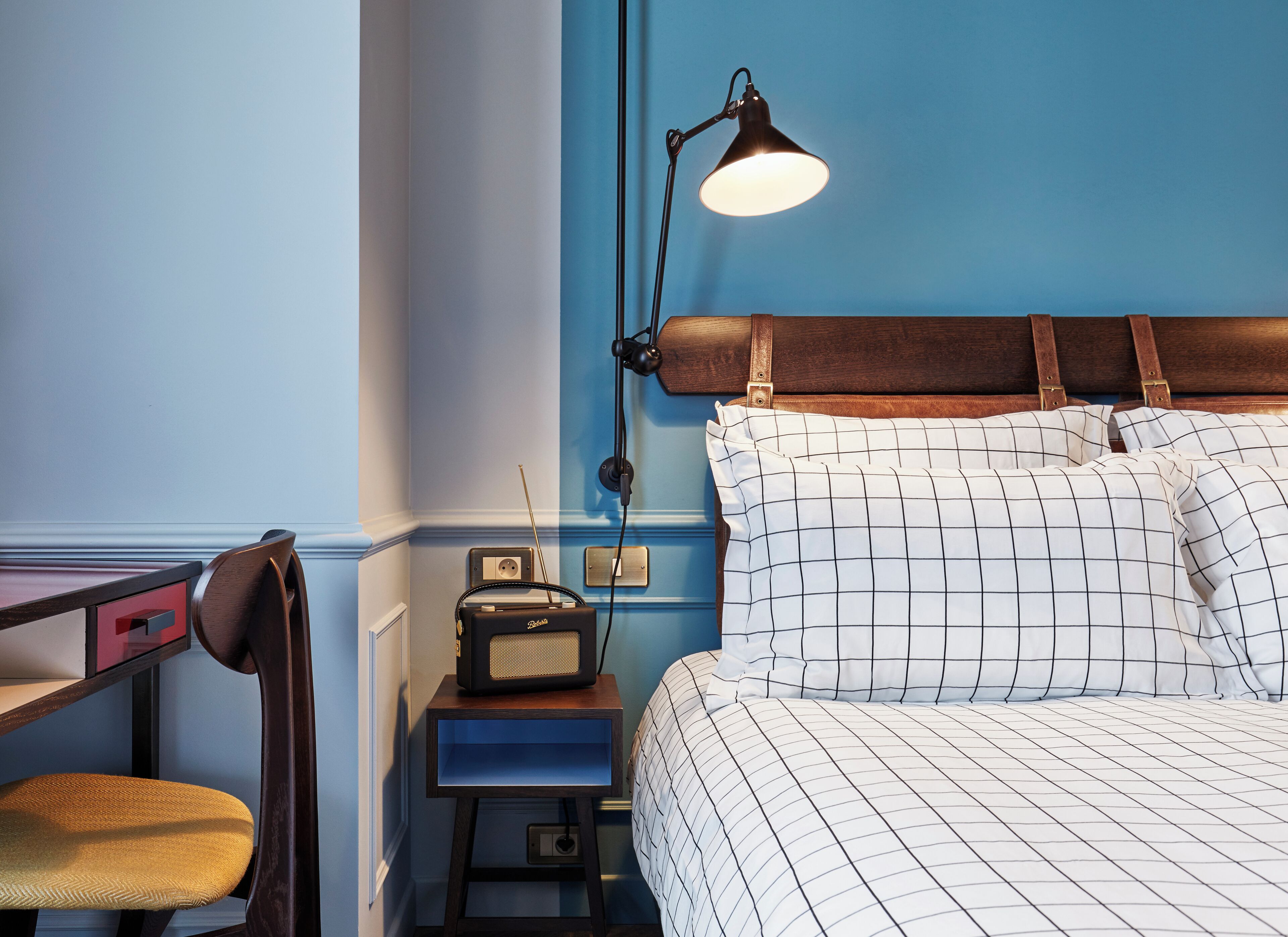A room with a bed, a desk, a chair, a lamp, and a vintage radio.