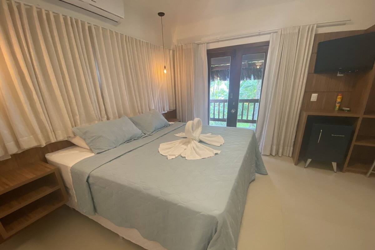 A hotel room with a bed, a TV, a minibar, and a view of the outdoors.