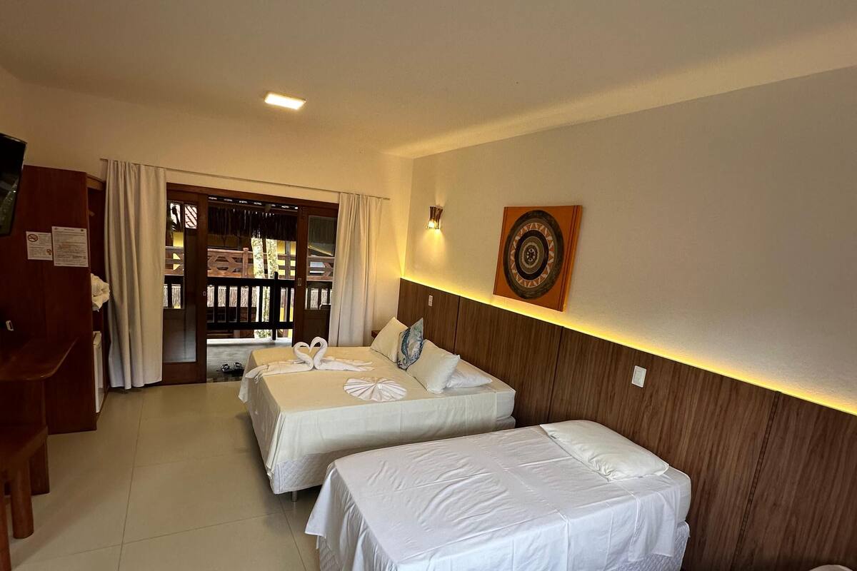 A hotel room with two single beds, a wooden headboard, a wall-mounted clock, and a door leading to a balcony.