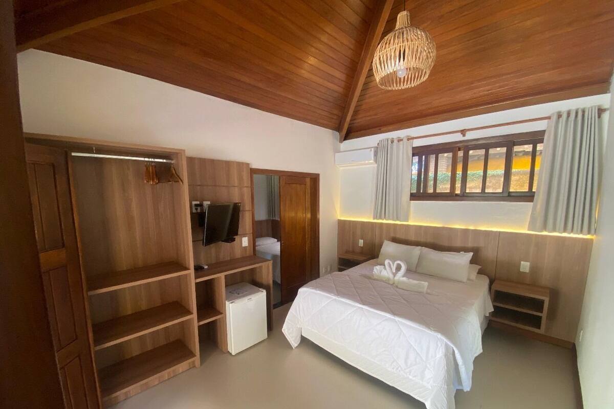 A bedroom with a large bed, wooden wardrobe, and a television.