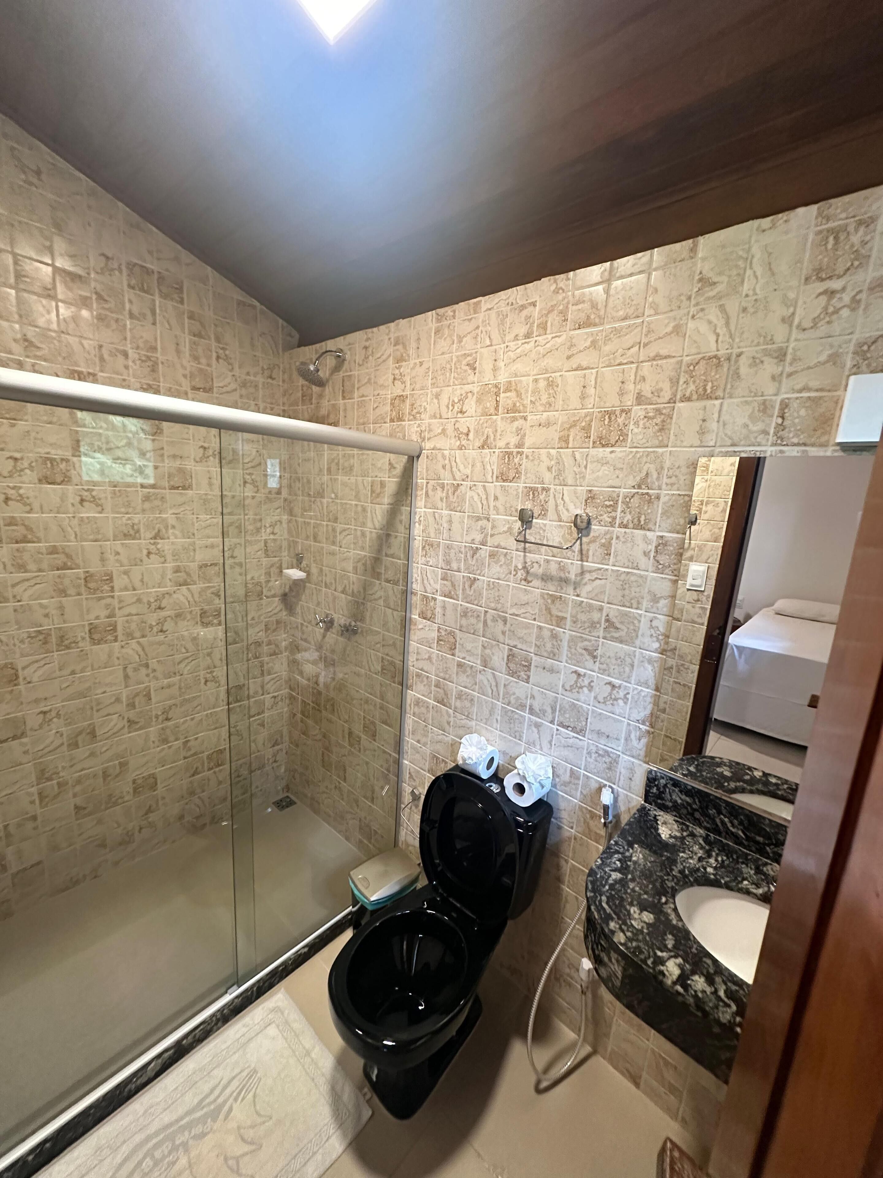 Casa de banho com chuveiro em cabine de vidro, sanita preta e lavatório de mármore.