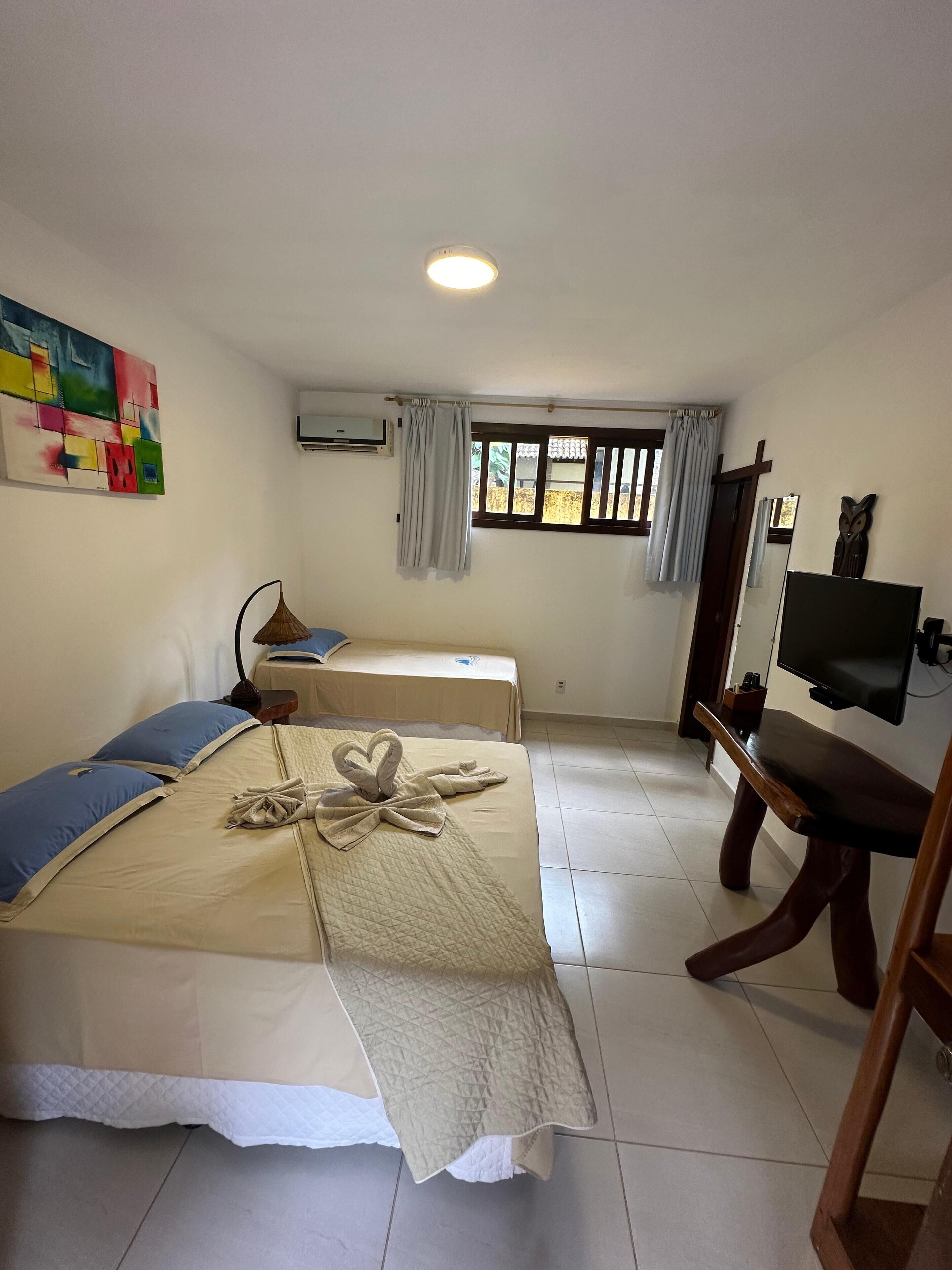 A hotel room with two beds, a TV, a window with curtains, and a colorful abstract painting on the wall.