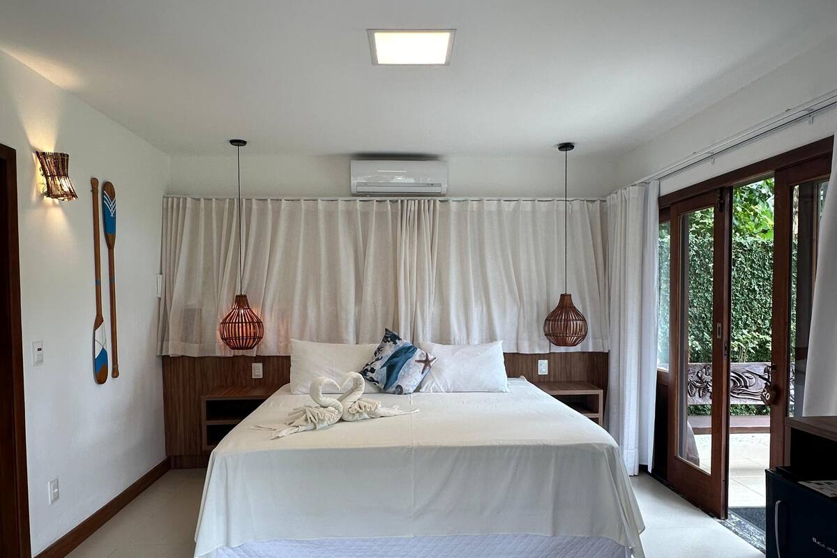 A spacious bedroom with a large bed, a ceiling fan, an air conditioning unit, and a view of the outdoors through a sliding glass door.