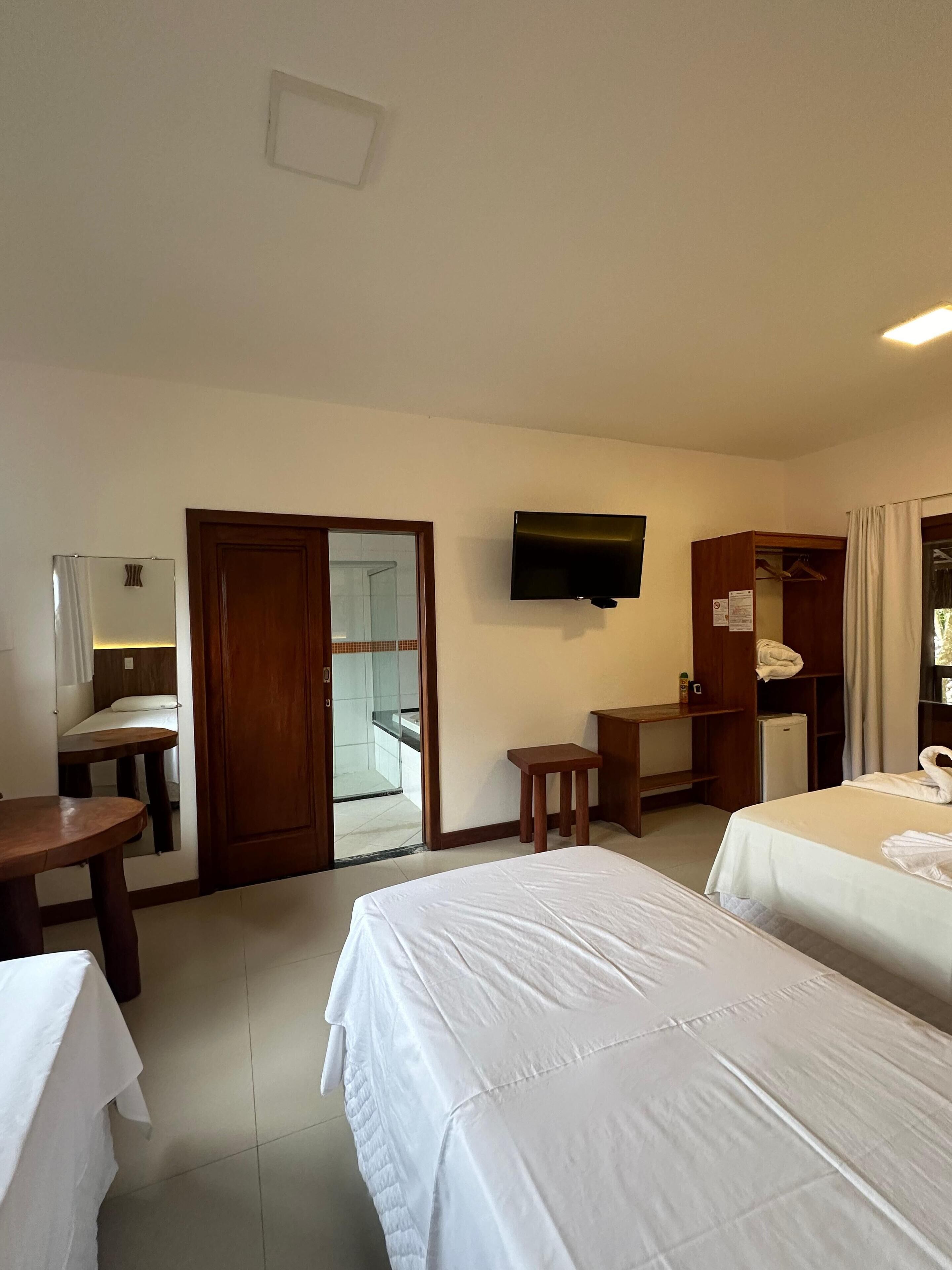 Ein Hotelzimmer mit zwei Betten, einem Schreibtisch, einem Fernseher, einem Kleiderschrank und einem durch eine offene Tür einsehbaren Badezimmer.