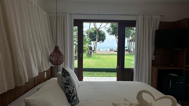 Camera d'albergo con un letto, una TV e vista su una zona verde con alberi e uno specchio d'acqua.