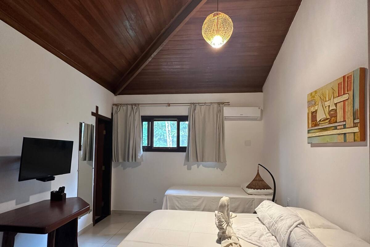 A bedroom with a large bed, a television, a desk, and a window with curtains.