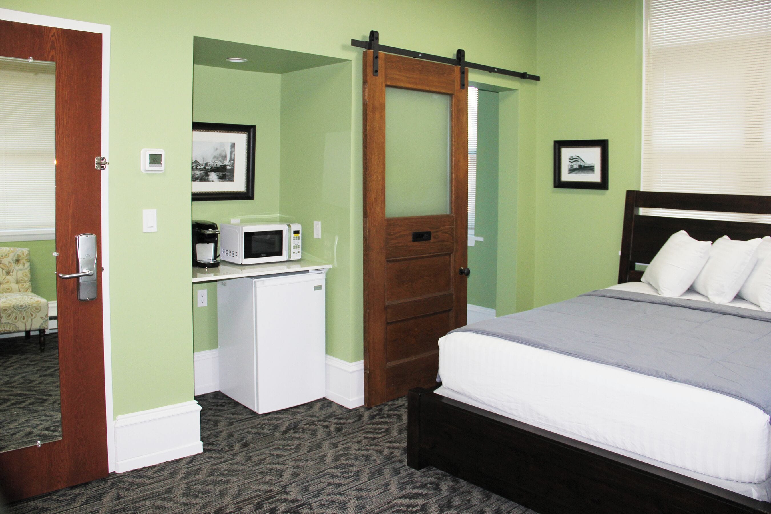 A hotel room with a bed, a desk with a microwave, a door, and a framed picture on the wall.
