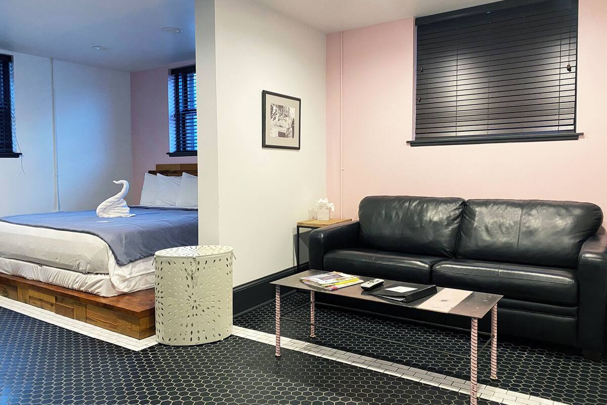 Een slaapkamer met een bed, een zwarte leren bank, een tafeltje en een foto aan de muur.