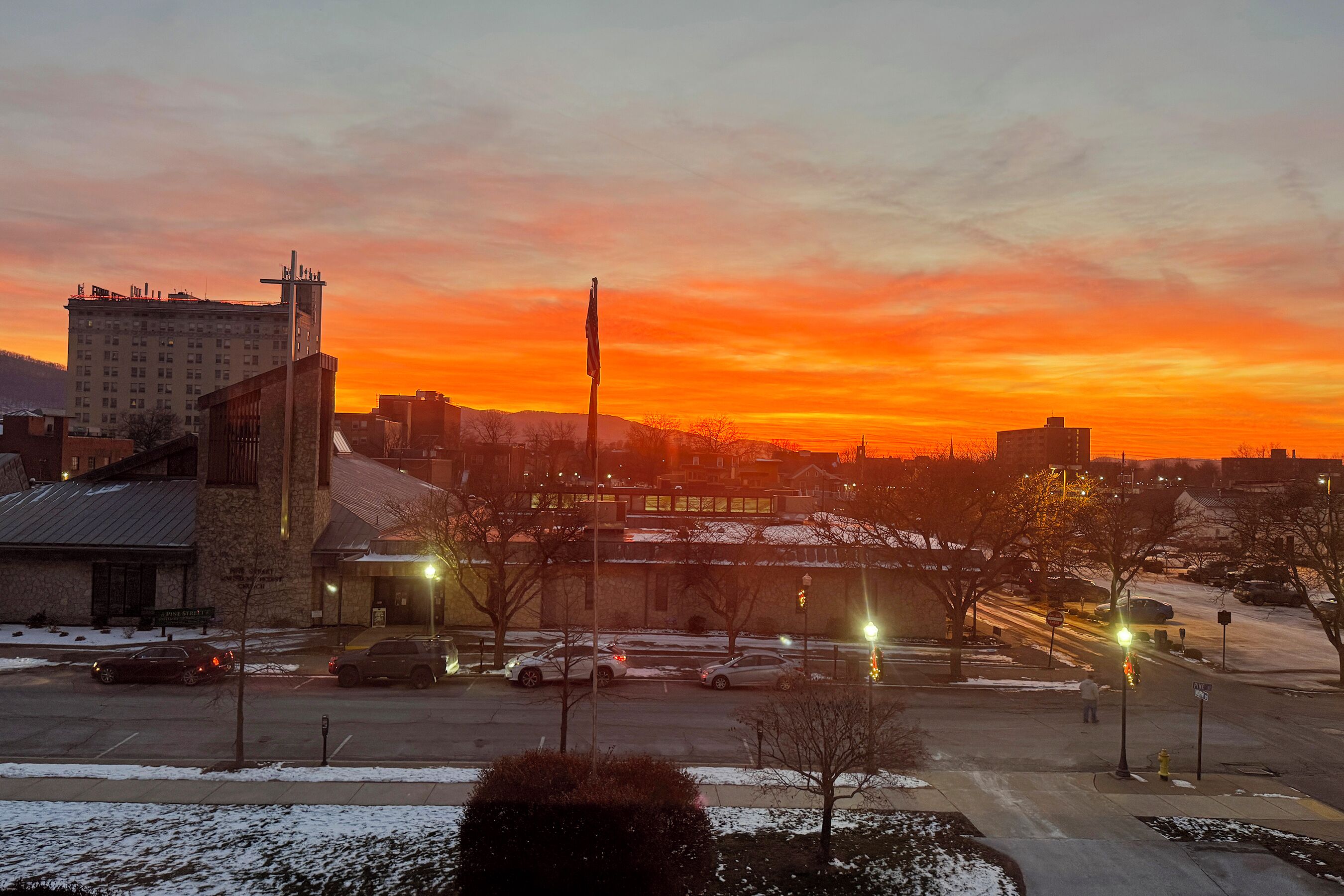 A parking lot with several cars, a building with a sign, and a sunset in the background.