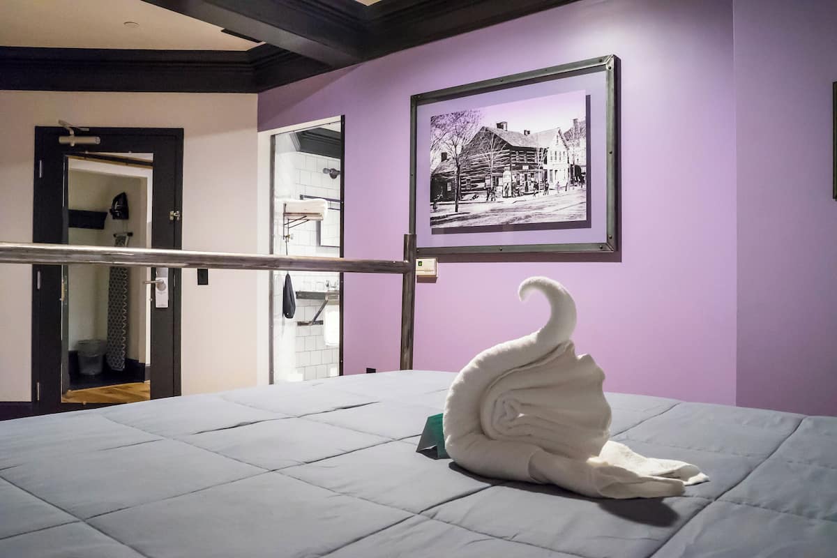 Een hotelkamer met een bed, een zwart-wit foto in een lijst aan de muur, en een handdoek in de vorm van een zwaan op het bed.