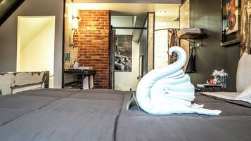 A hotel room with a neatly made bed, a brick wall, a bathroom with a mirror, and a painting on the wall.