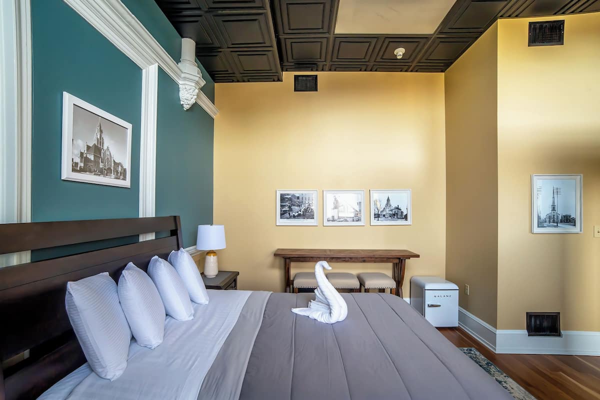 Een hotelkamer met een bed, een nachtkastje, een lamp, een tafeltje en een wandheater.
