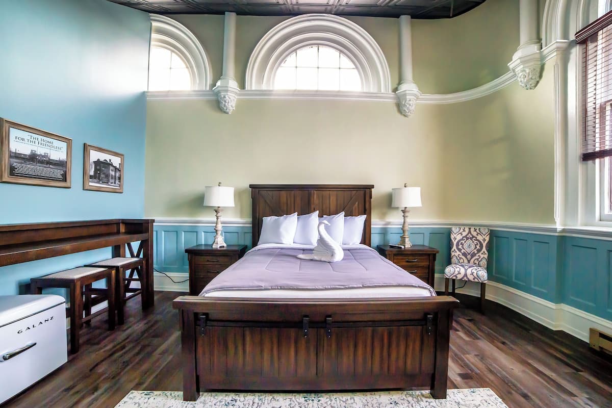 Een slaapkamer met een houten bed, twee nachtkastjes met lampen, een bankje en een dressoir.