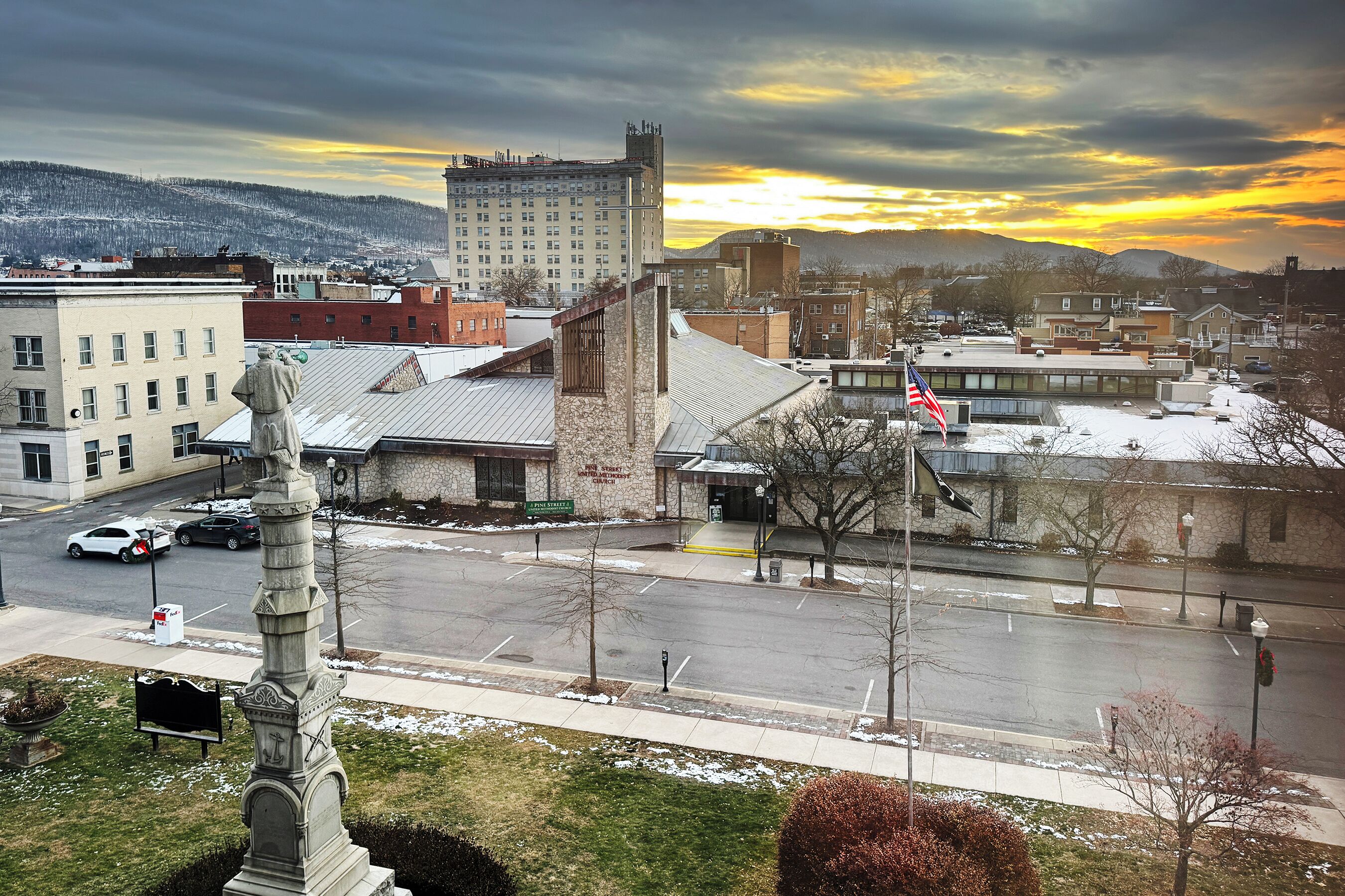 A downtown area with a mix of modern and historic buildings, a statue, and a parking lot.