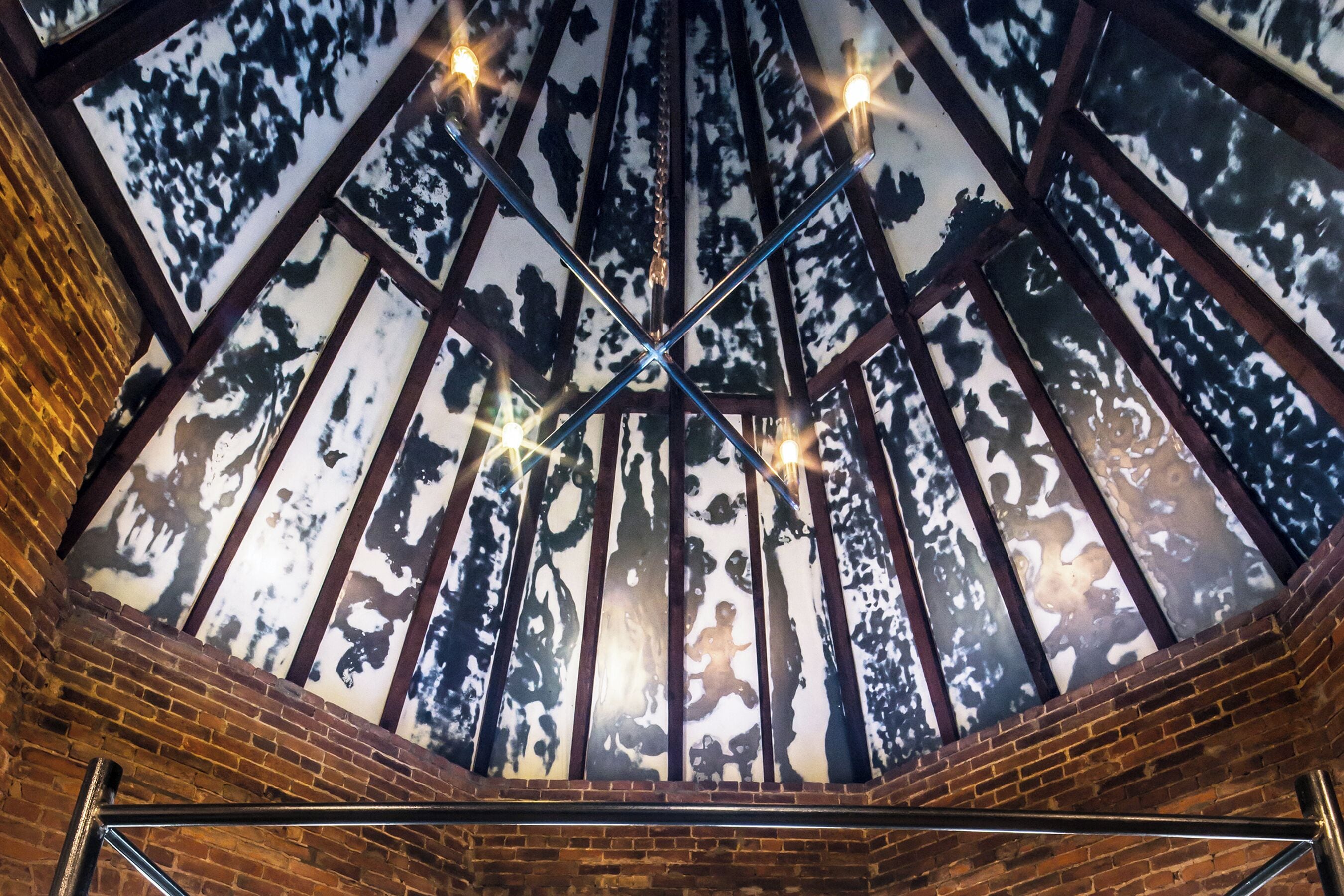 Una habitación con techo alto, vigas de madera y tragaluz con diseño de bosque.