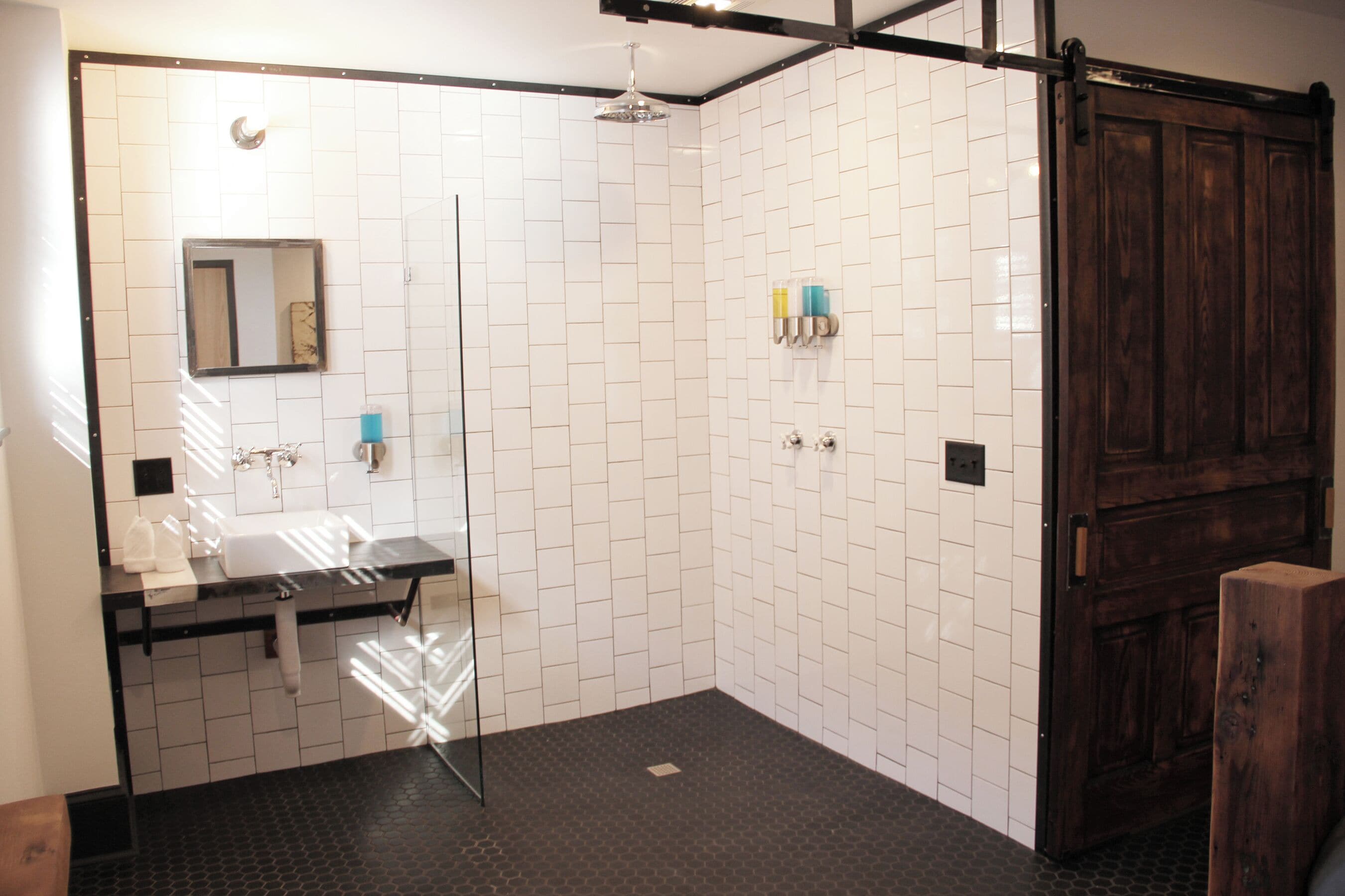 A modern bathroom with white tiled walls, a glass shower enclosure, and a wooden door.