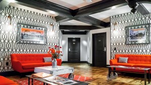 Een moderne lobby met twee oranje banken, een bijzettafeltje en een behang met een patroon.