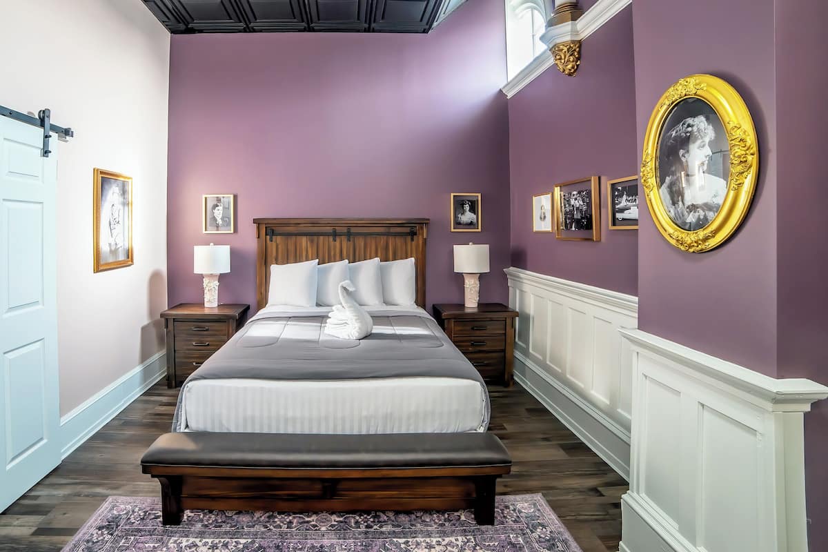 Een slaapkamer met een groot bed, twee nachtkastjes, een bankje en een muur met ingelijste foto's.