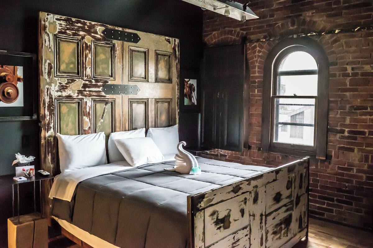 Een bed met een rustiek hoofdbord, een kussen in de vorm van een zwaan en een dressoir met een gebruikte afwerking.