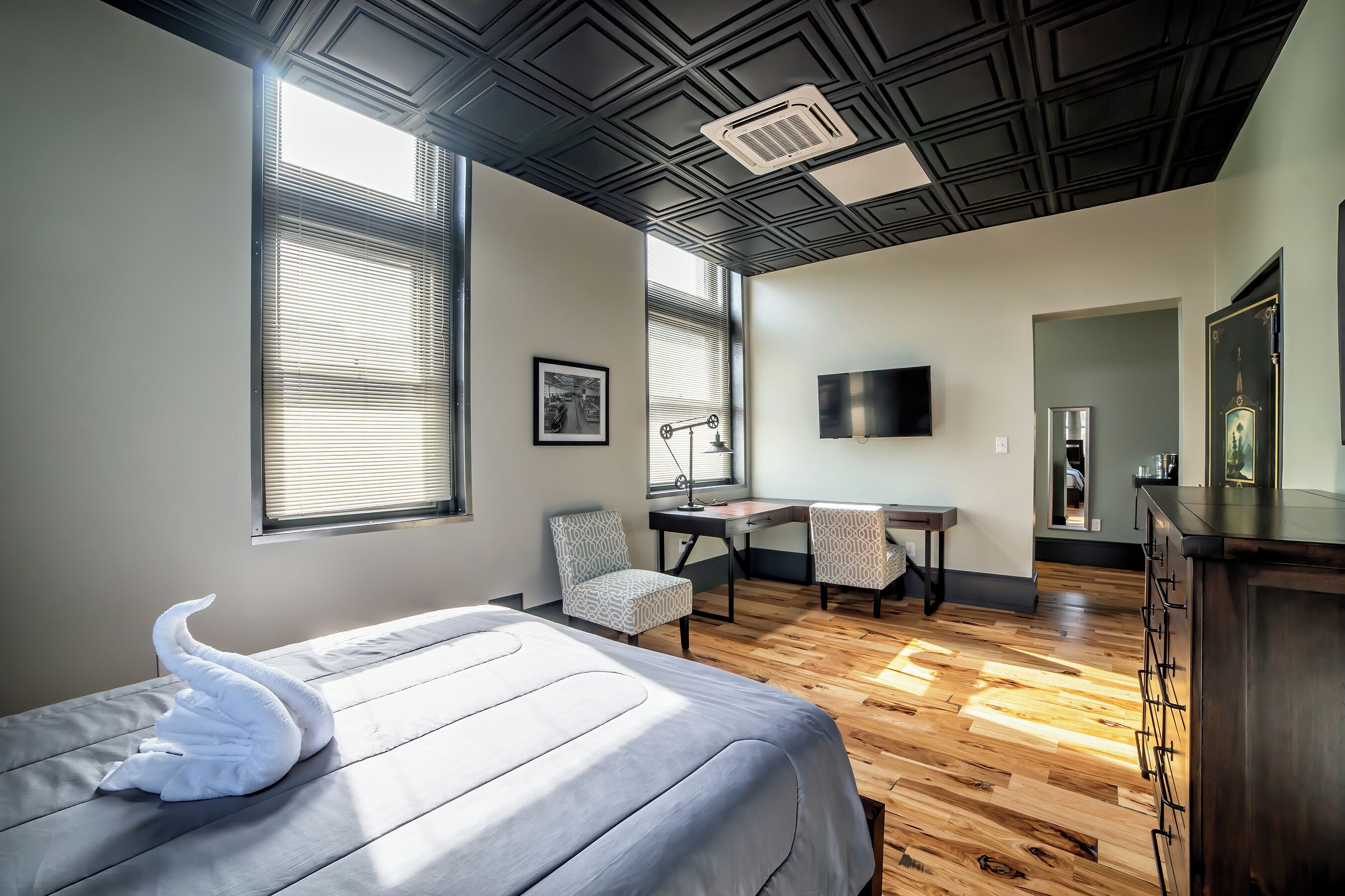 A modern hotel room with a bed, two chairs, a desk, a TV, and a dresser.