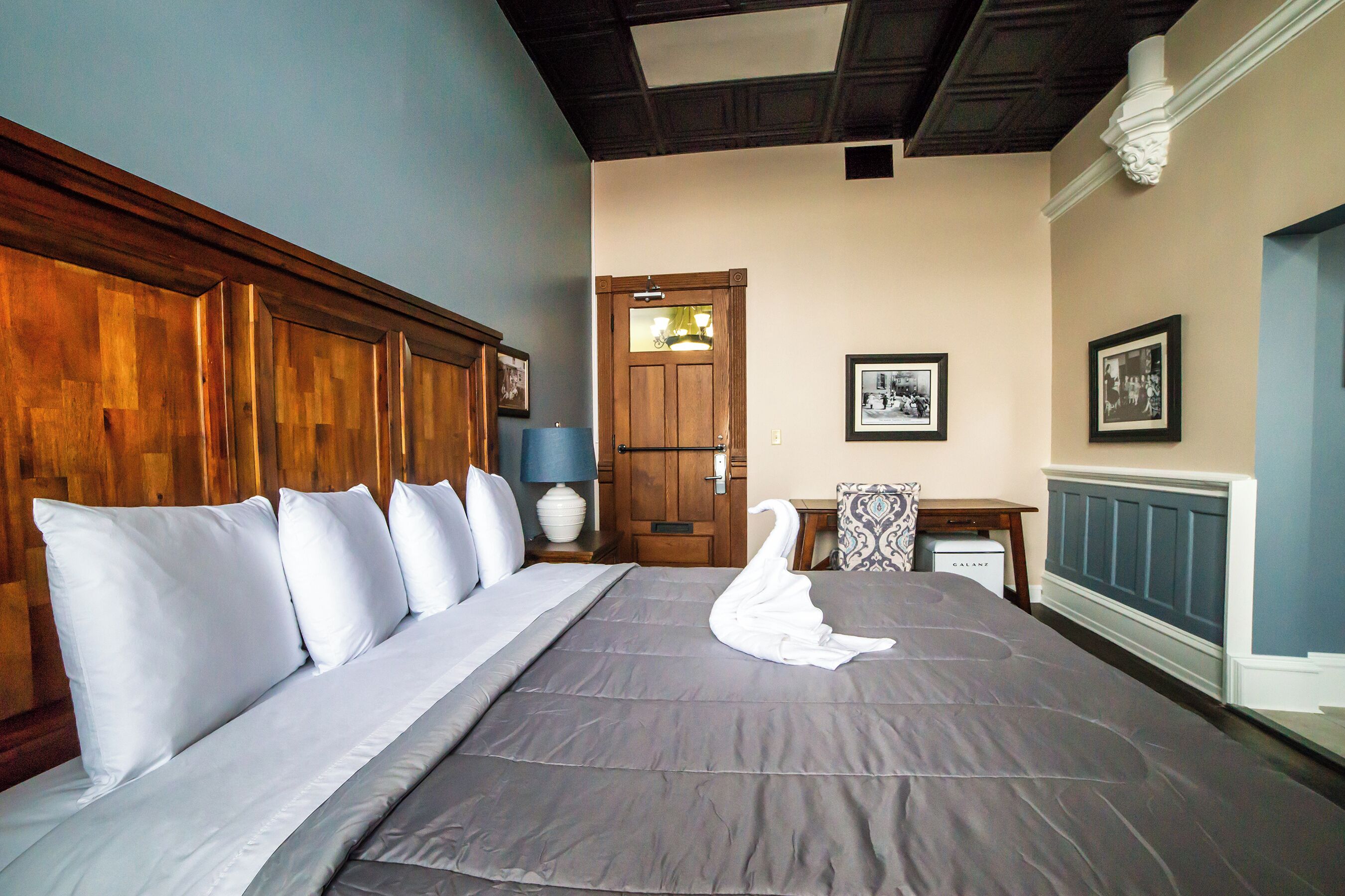 A neatly made bed with a swan-shaped towel, a wooden headboard, and a nightstand with a lamp.