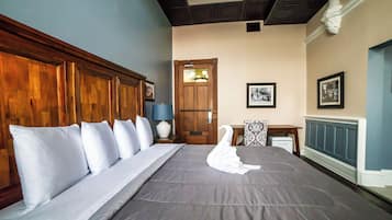 A neatly made bed with a swan-shaped towel, a wooden headboard, and a nightstand with a lamp.