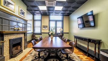 A conference room with a large wooden table, chairs, a fireplace, and a television on the wall.