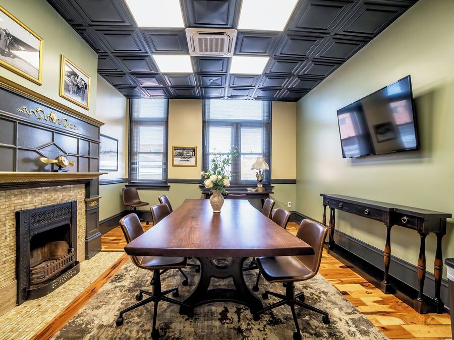 A conference room with a large wooden table, chairs, a fireplace, and a television on the wall.